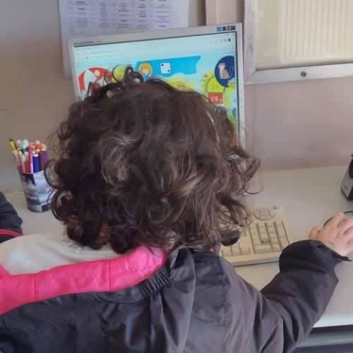 Παιδί κάθεται μπροστά από υπολογιστή σε σχολική αίθουσα και παίζει το παιχνίδι «Ταξιδιώτες»