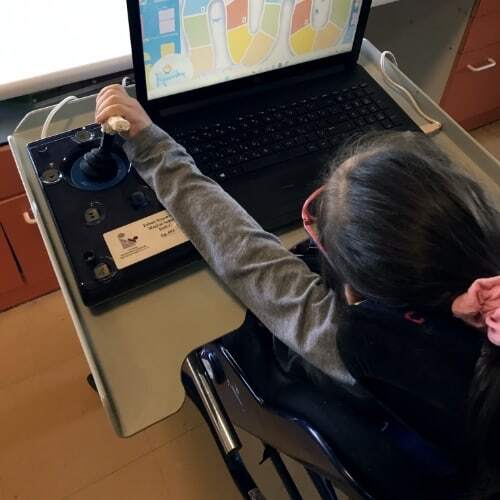Παιδί που κάθεται μπροστά από φορητό υπολογιστή και παίζει το παιχνίδι «Ταξιδιώτες» με τη βοήθεια ειδικού μοχλού